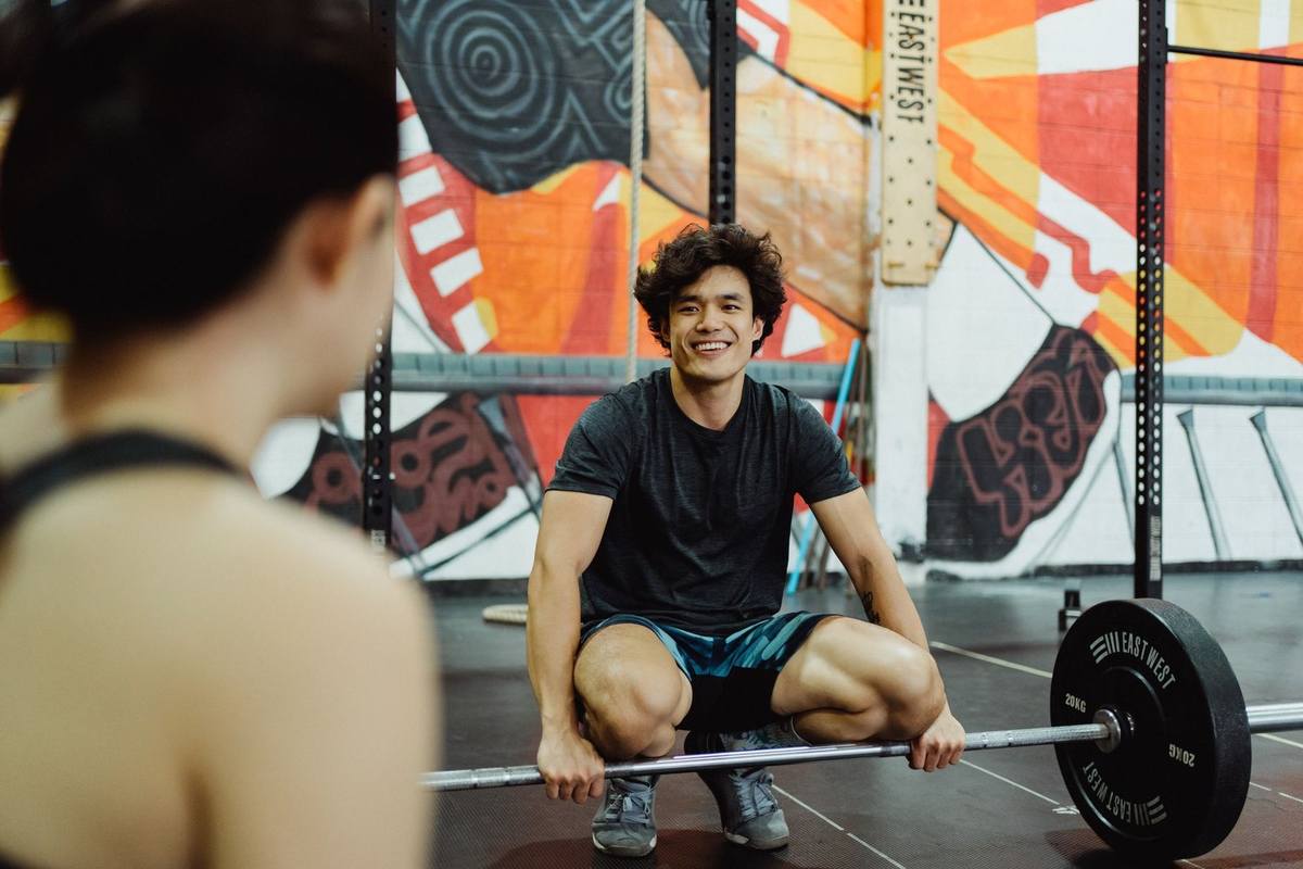 Homme musclé en squat avec barre de haltères dans une salle de musculation