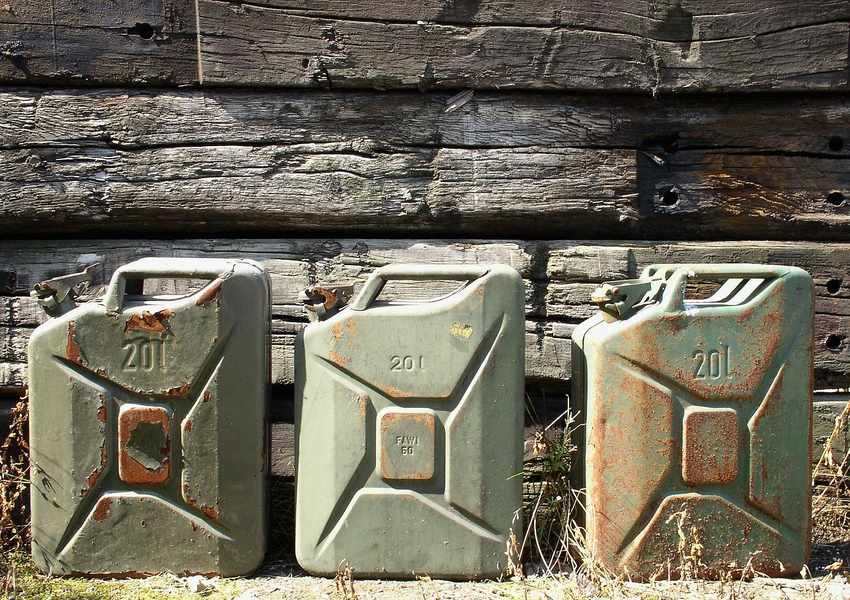Trois bidons métalliques de vingt litres rouillés et usés posés contre des planches en bois